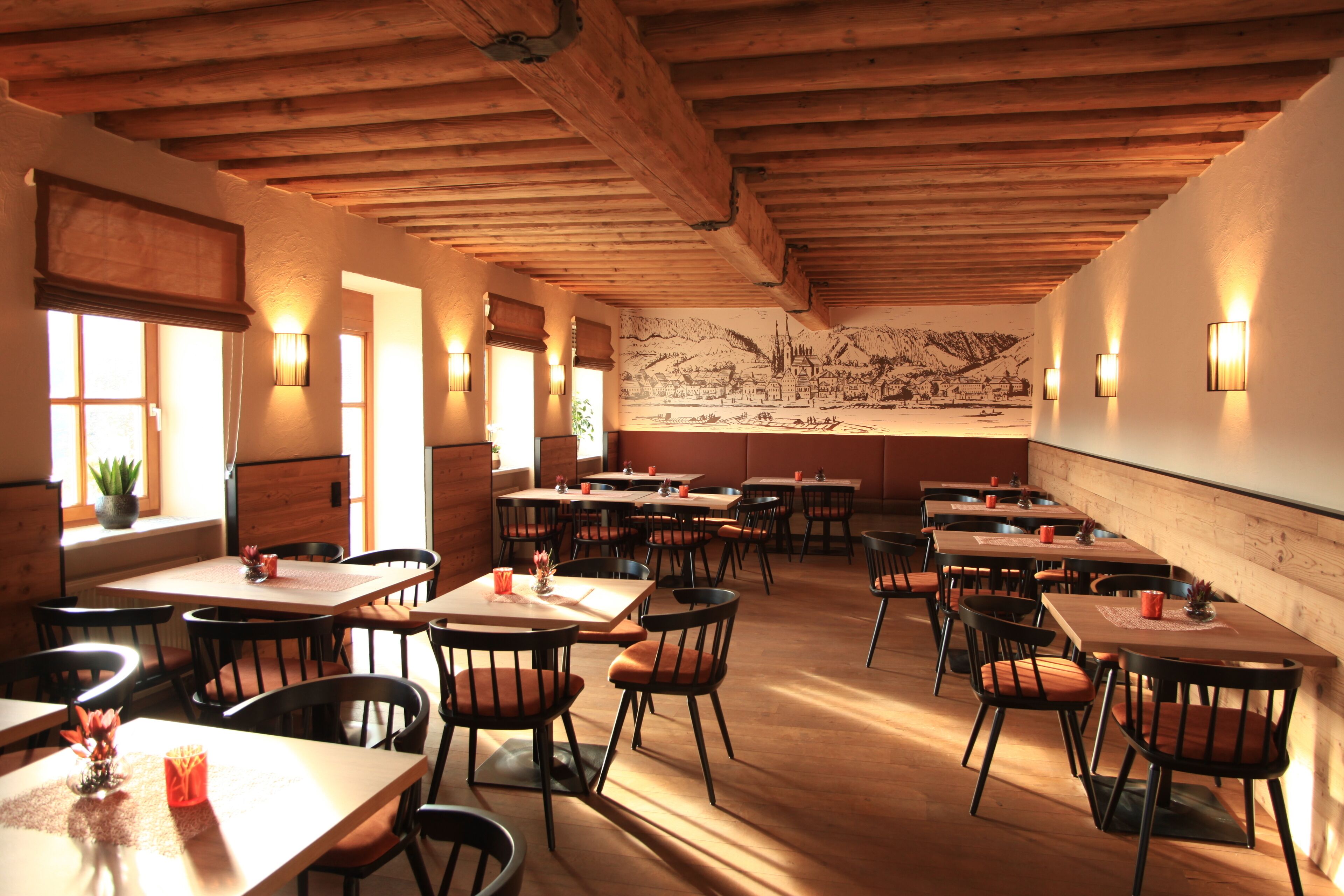 A restaurant with wooden beams, tables, chairs, and wall-mounted lights.