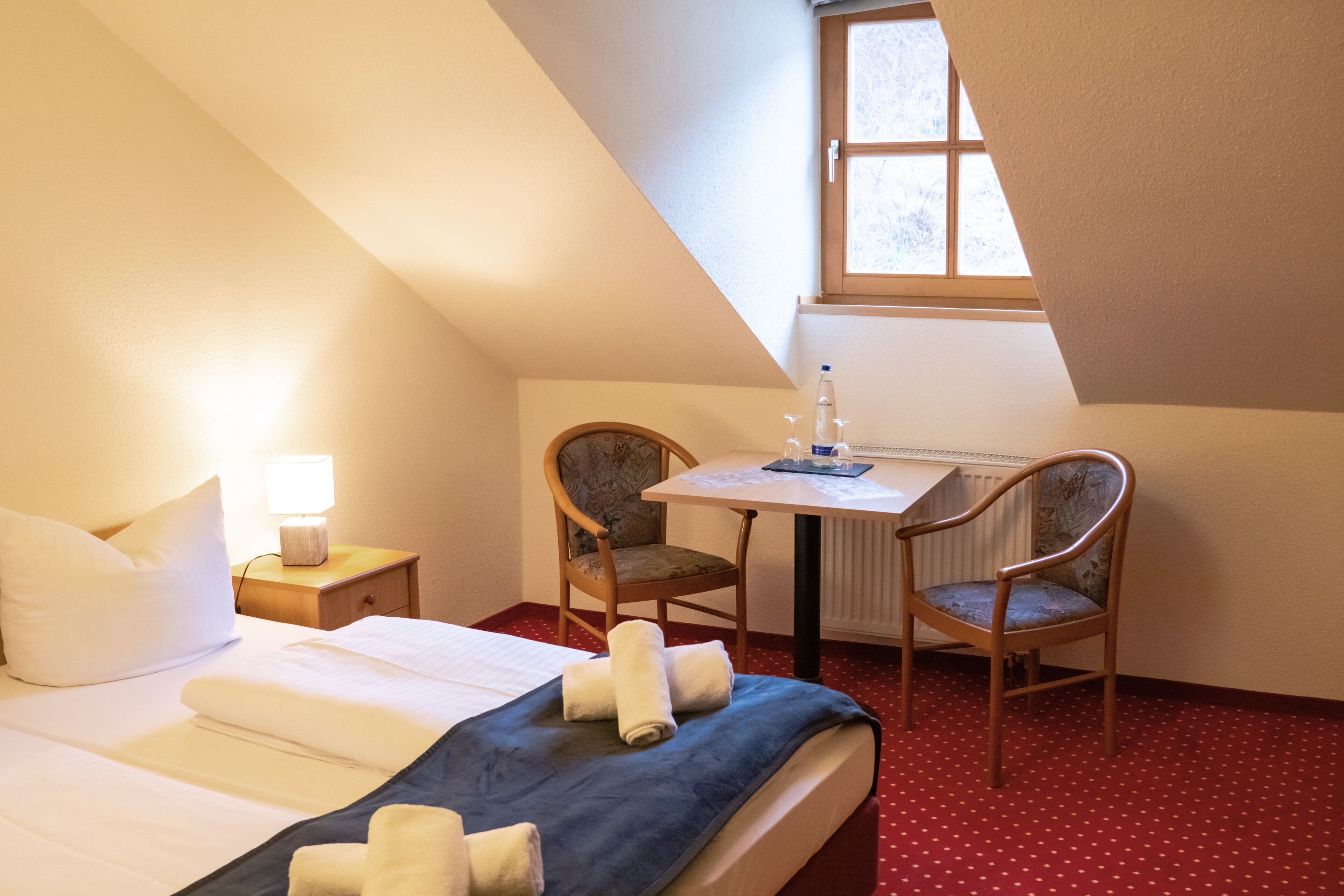 Ein Hotelzimmer mit Bett, zwei Stühlen, einem Tisch und einem Fenster.