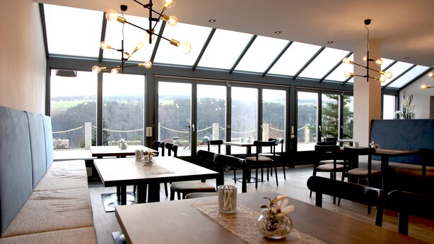 Un comedor moderno con techos altos, ventanas amplias y vistas a un paisaje boscoso.