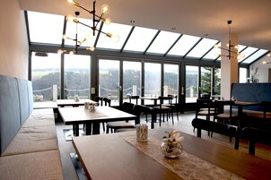 Un comedor moderno con techos altos, ventanas amplias y vistas a un paisaje boscoso.