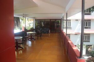 A covered outdoor area with a wooden floor, tables, chairs, and a bar area.