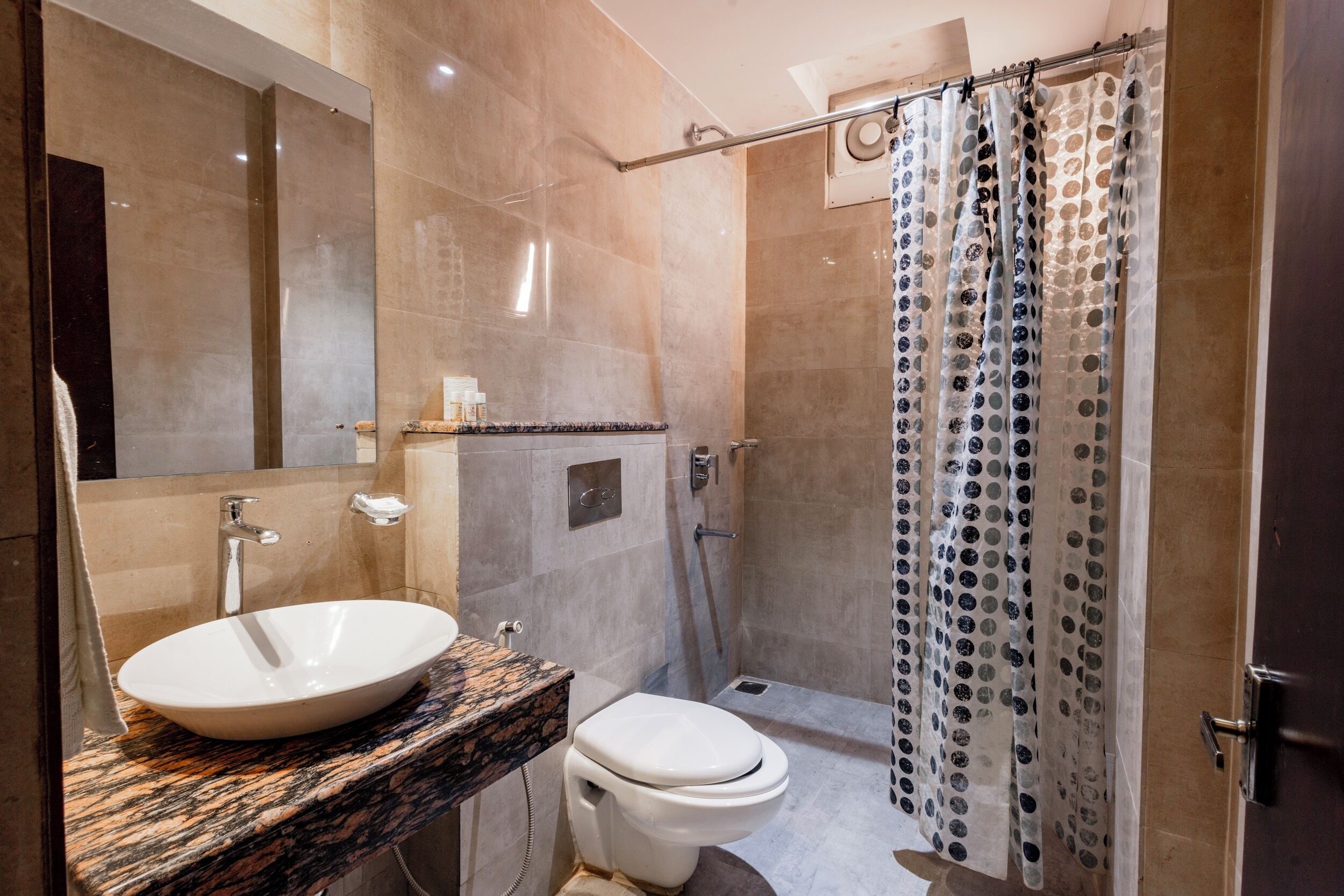 A bathroom with a marble sink, a toilet, and a shower with a patterned curtain.