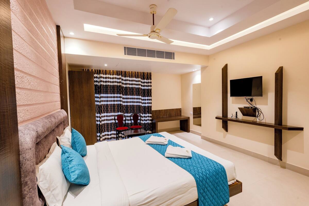 A modern hotel room with a large bed, a ceiling fan, a TV mounted on the wall, and a small desk with a chair.