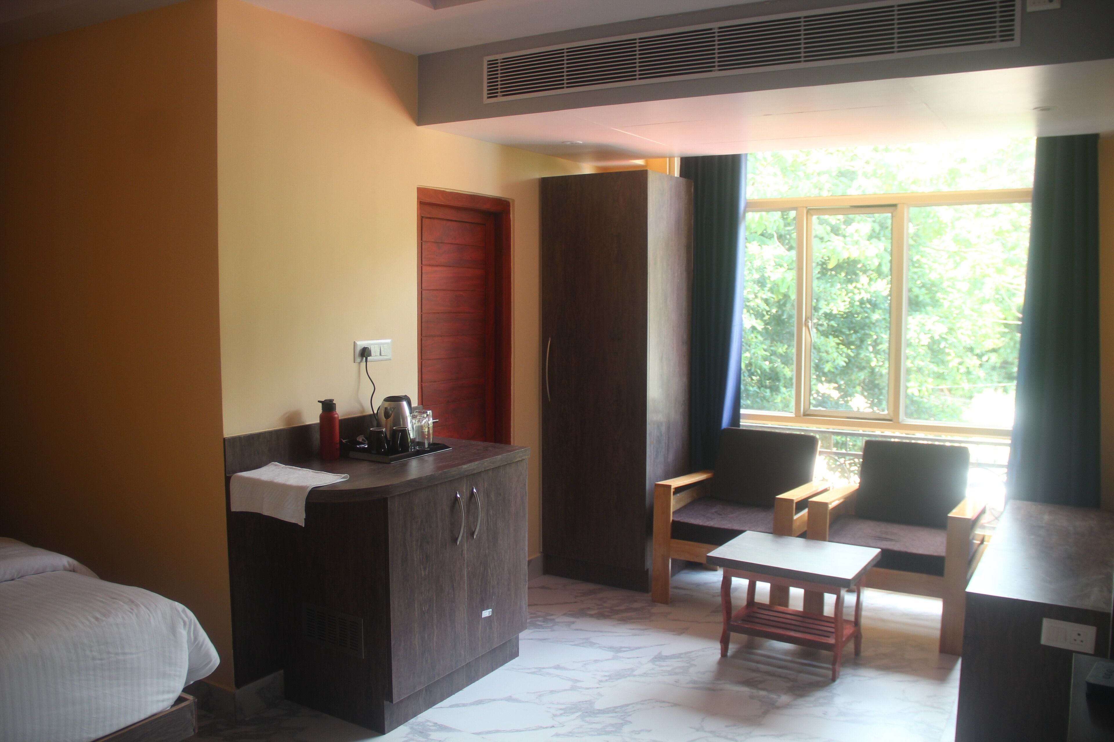 Hotelkamer met een bed, een houten bureau, een stoel, een kast en een raam met uitzicht op bomen.