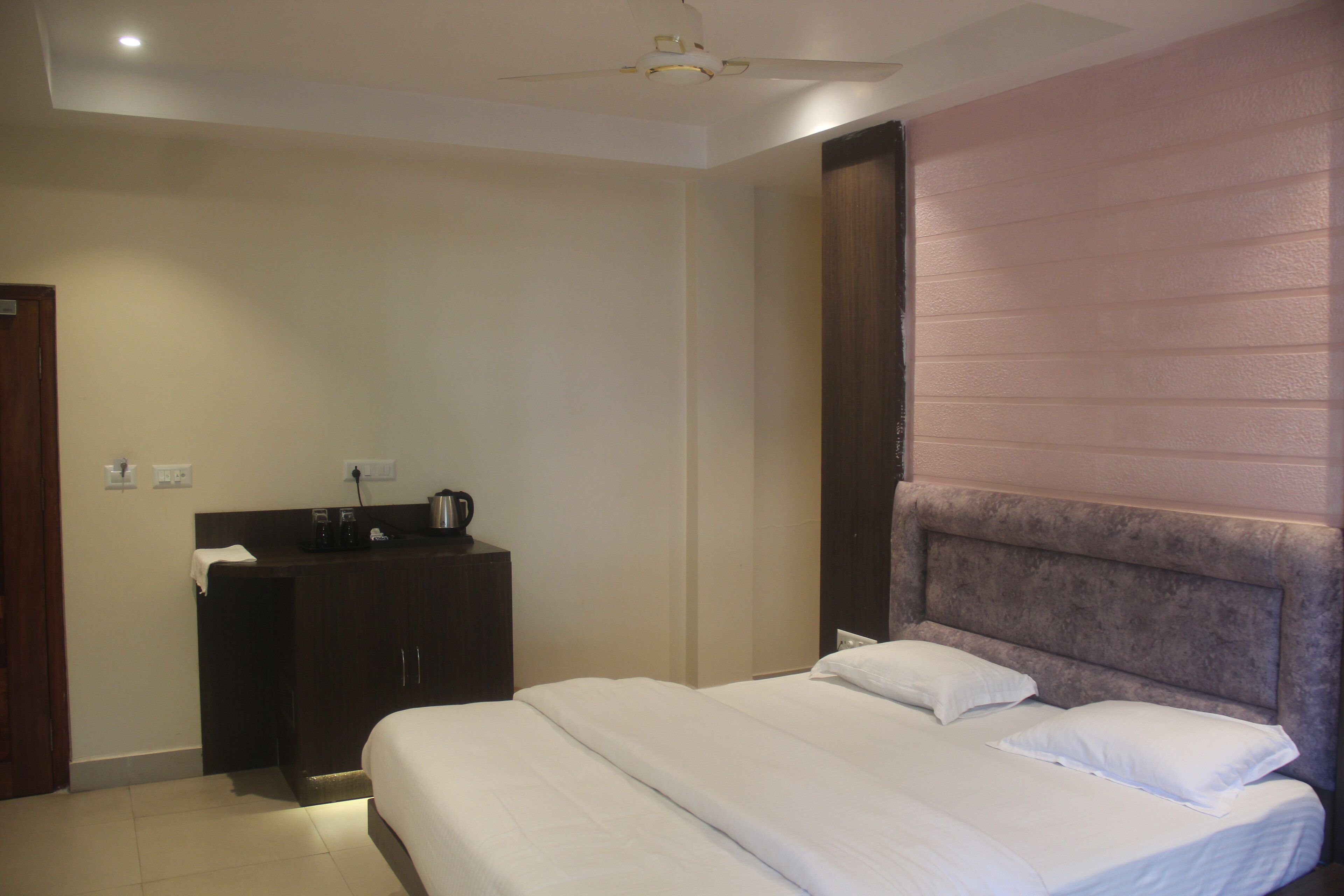 Una habitación de hotel con cama, mesita de noche, cafetera y ventilador de techo.
