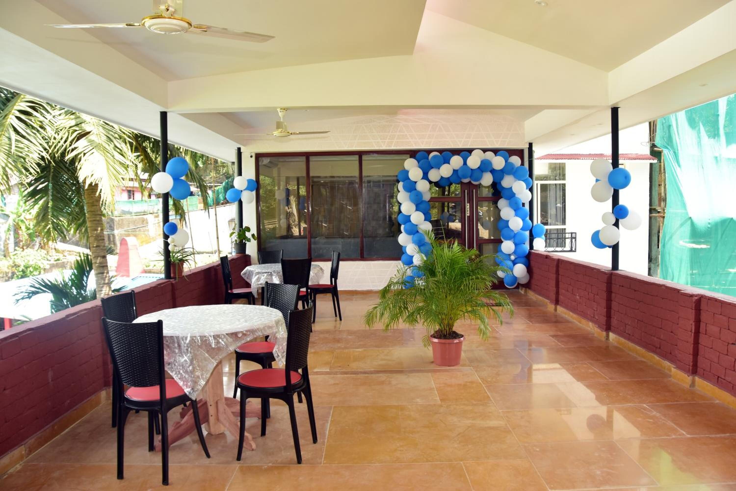 A covered outdoor dining area with tables and chairs, a ceiling fan, and a decorative balloon arch.