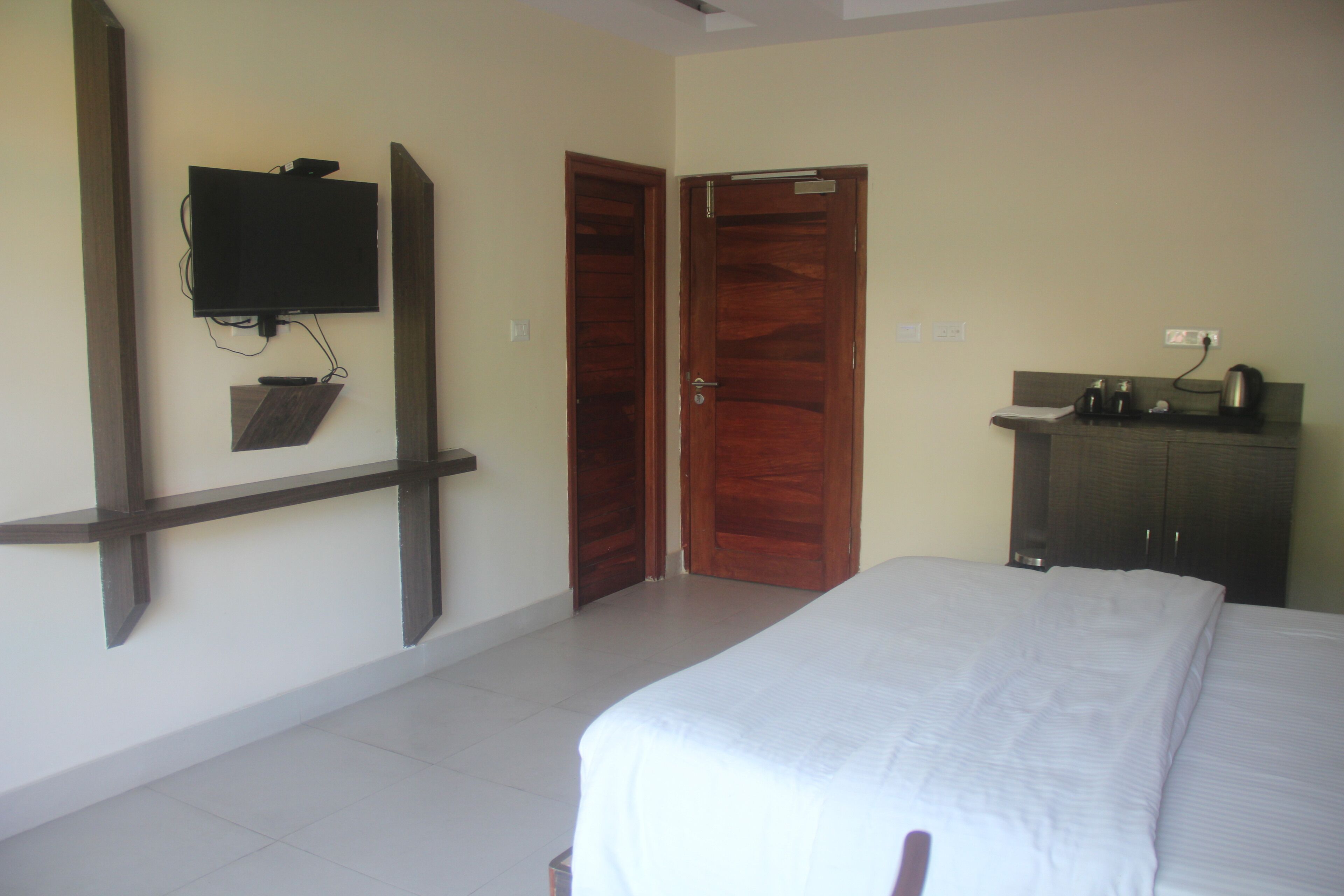 A bedroom with a bed, a TV mounted on the wall, a wooden wardrobe, and a door.