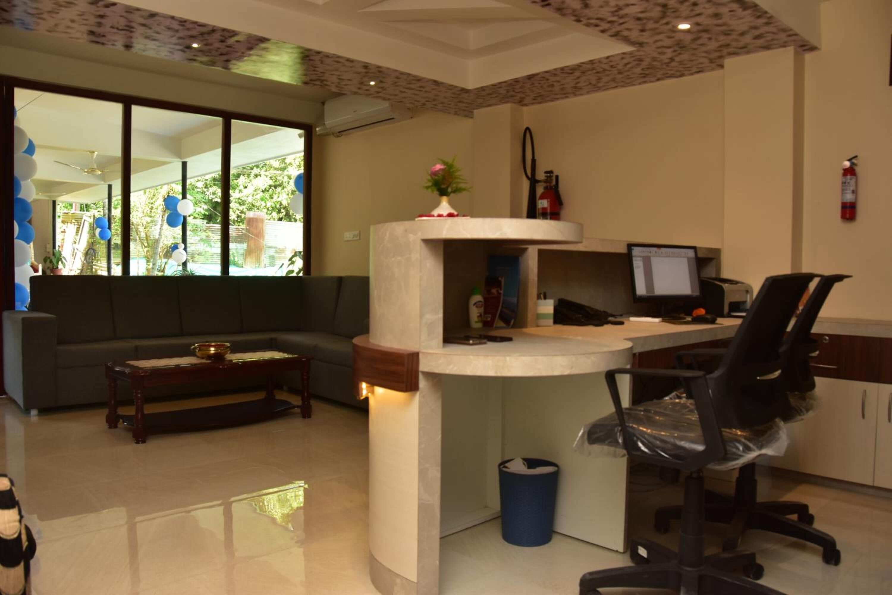 Un área de recepción con un mostrador curvo, una computadora, una silla de oficina negra, un sofá y una mesa de centro.