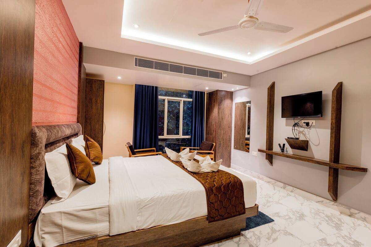 A modern hotel room with a large bed, a ceiling fan, a TV mounted on the wall, and a window with curtains.