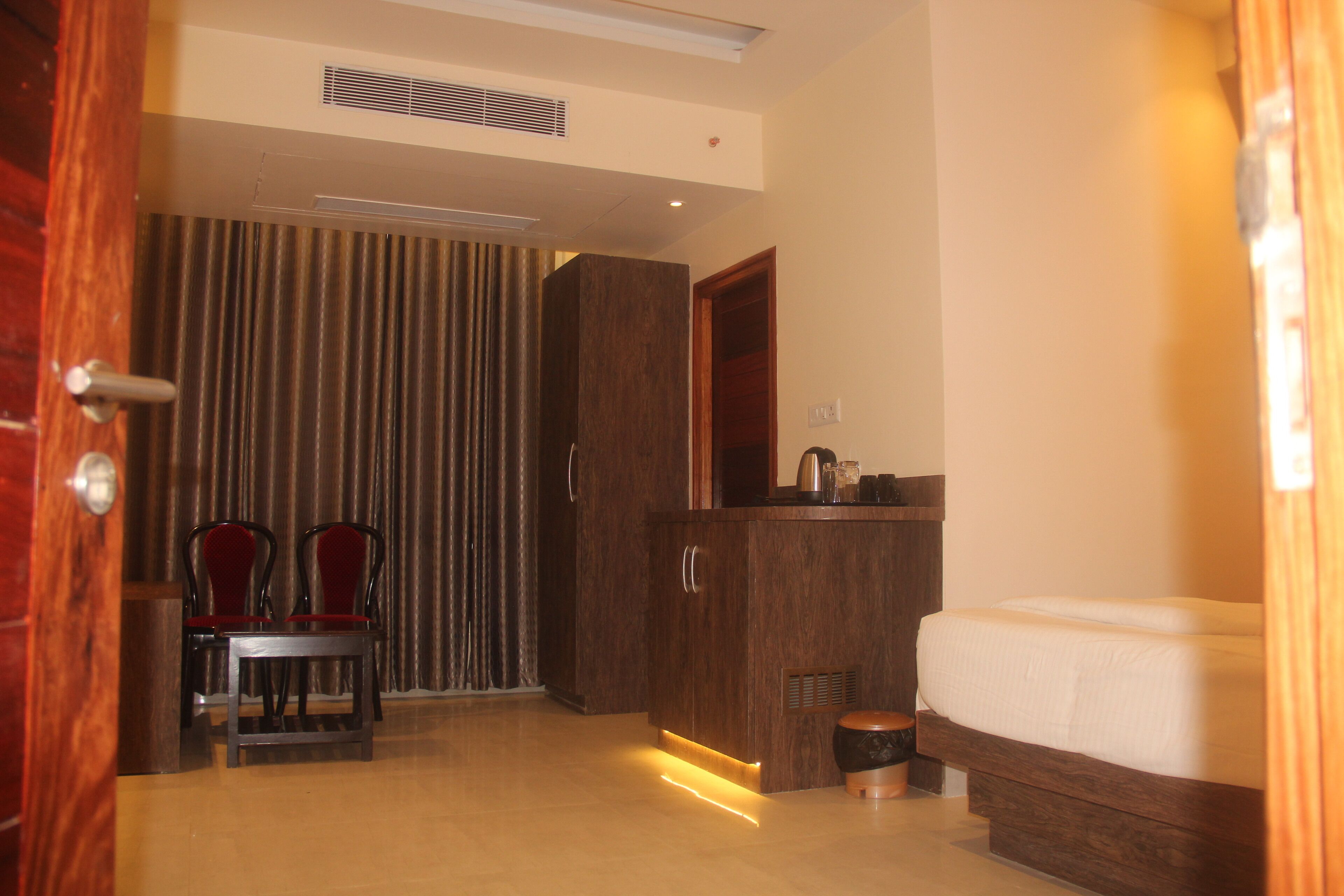 A hotel room with a bed, a wooden cabinet, a chair, and a curtain.
