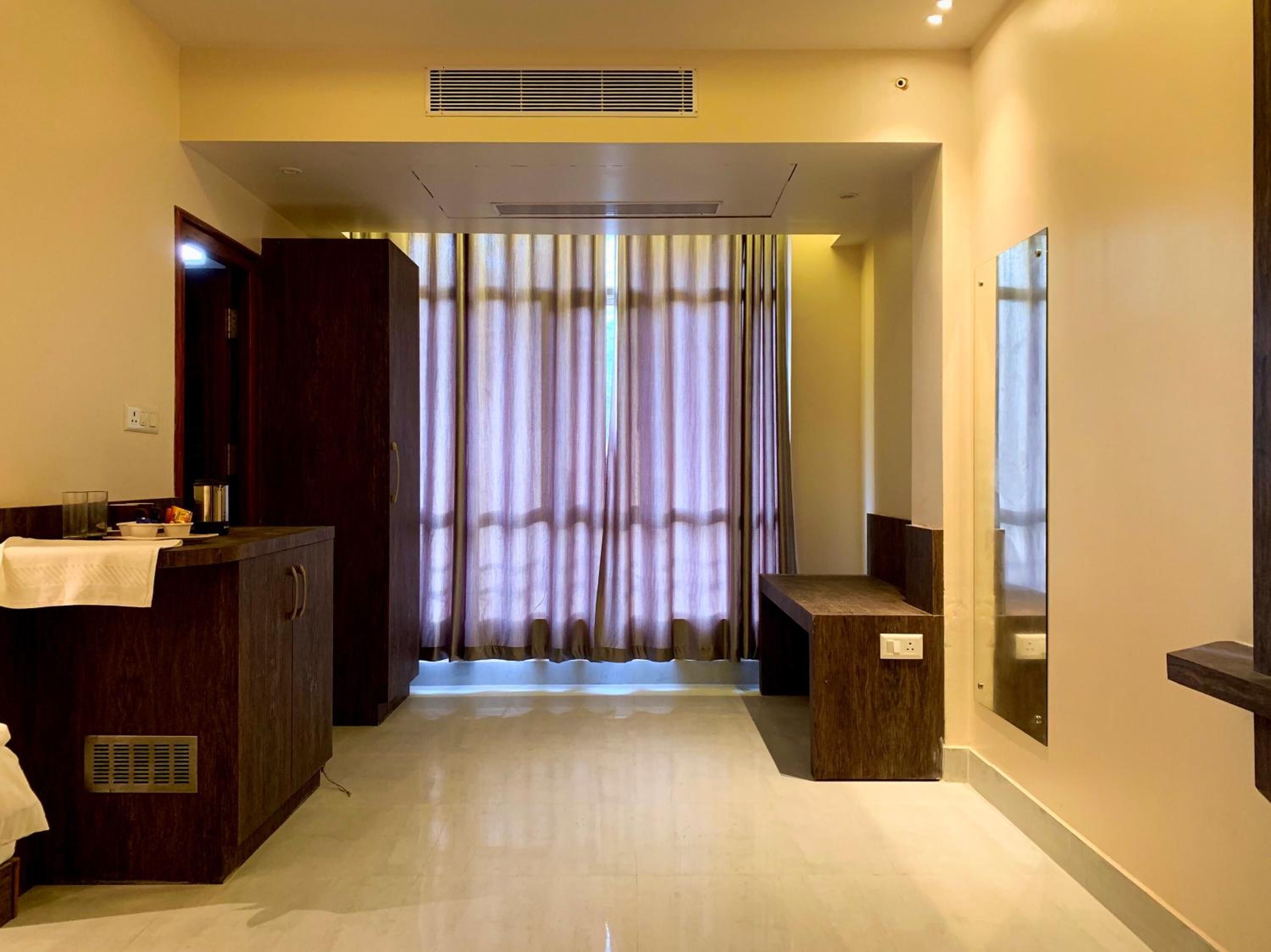 A hotel room with a wooden vanity, a mirror, a towel on the counter, and a view through a curtain.