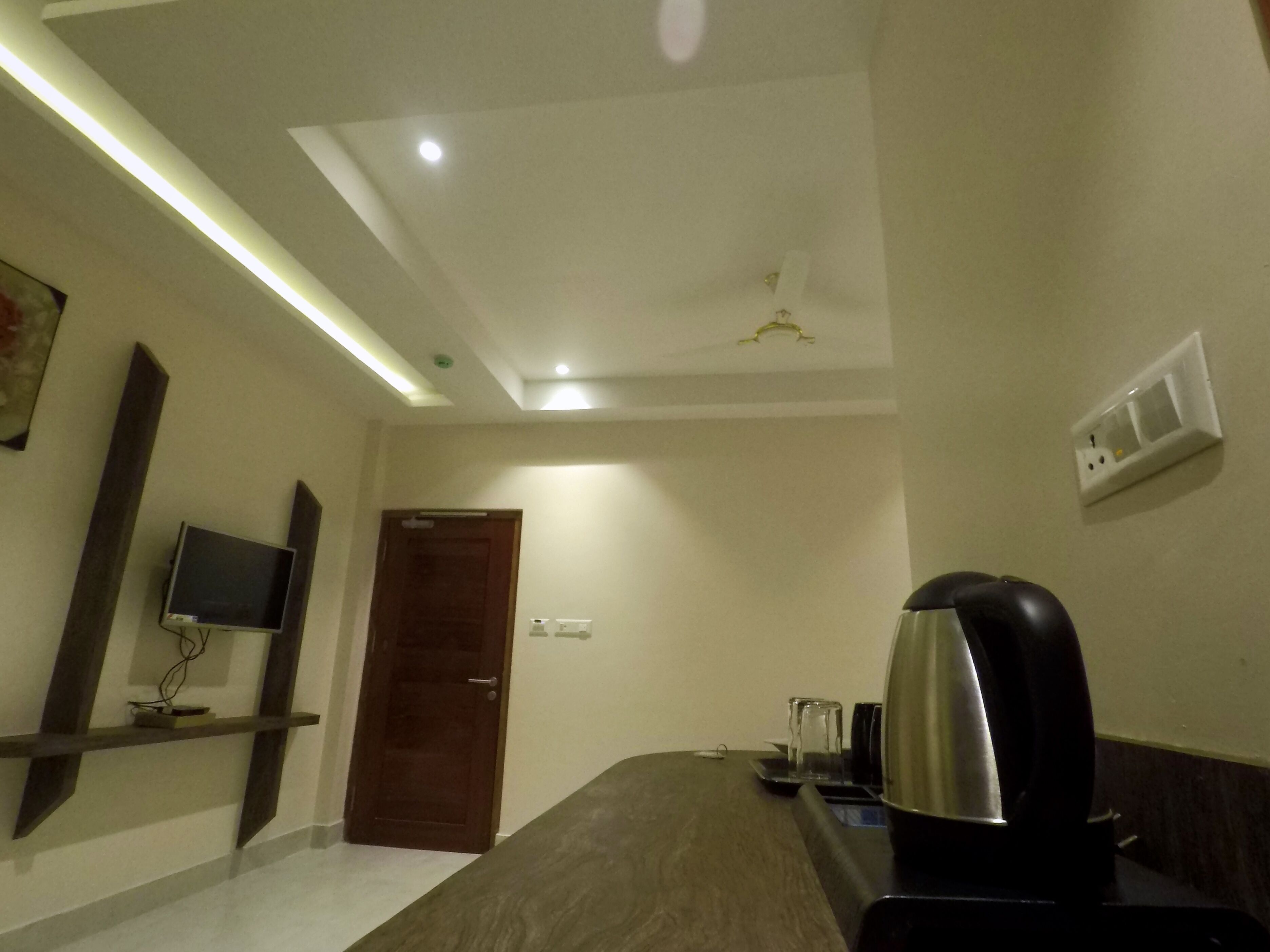 A hotel room with a bed, a TV mounted on the wall, a ceiling fan, and a power outlet on the wall.