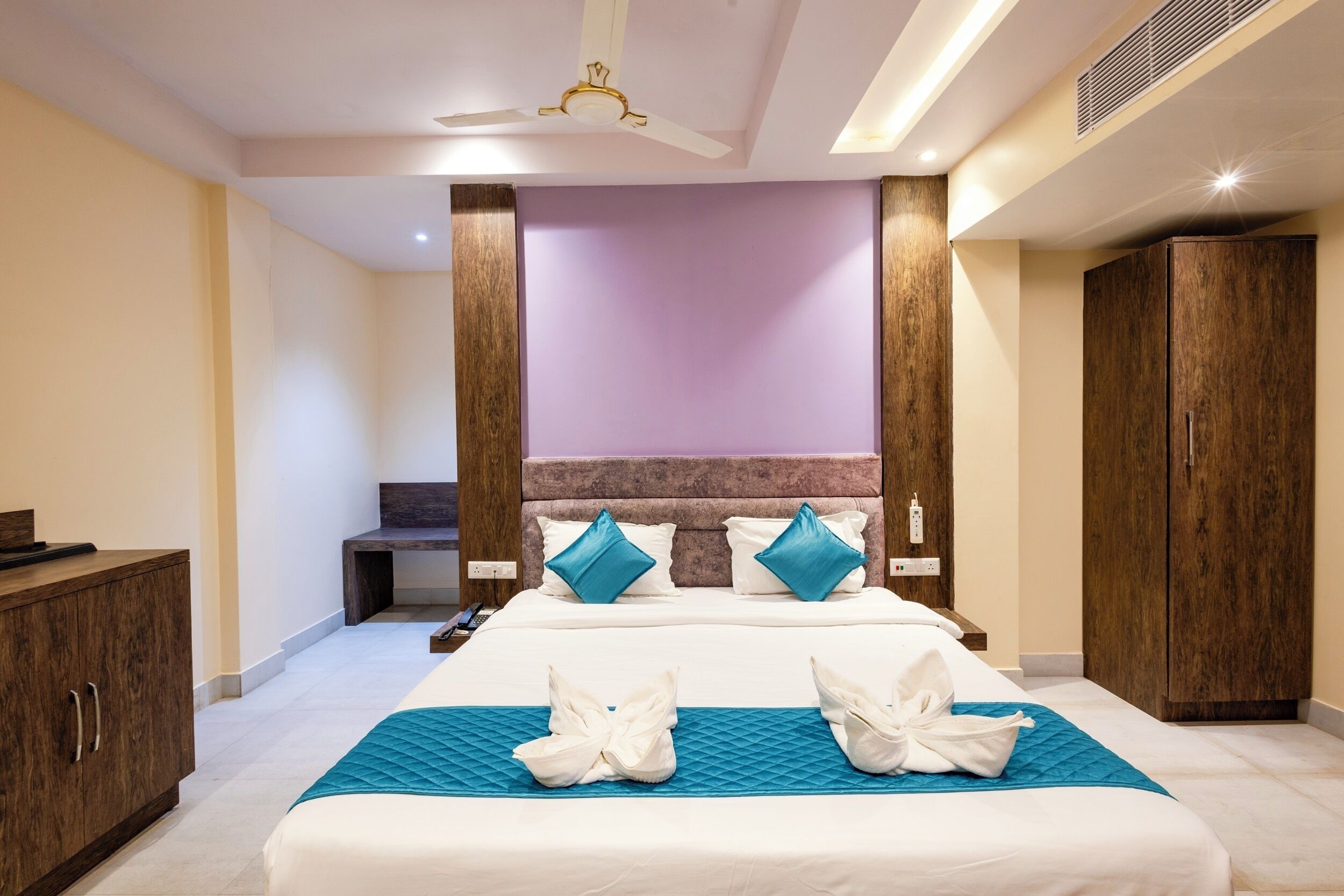 A hotel room with a large bed, wooden wardrobe, and a desk.