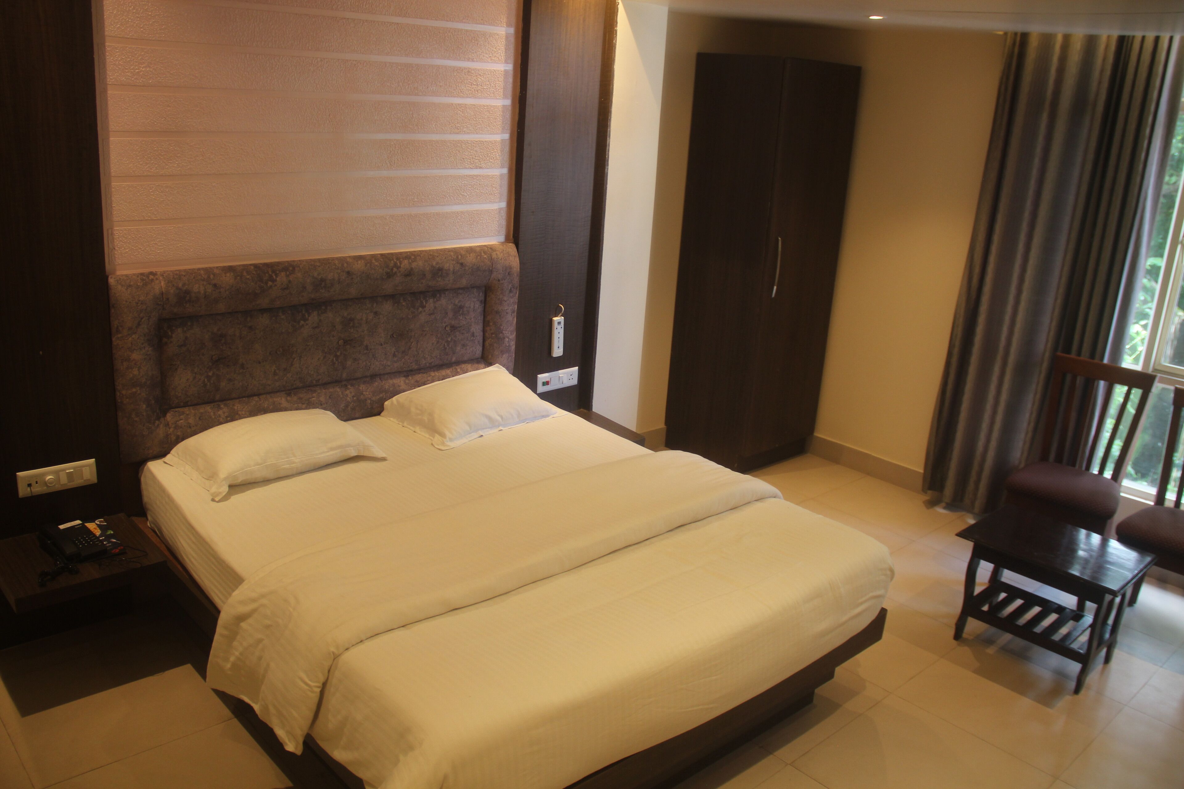 Une chambre d’hôtel avec un grand lit, une table de chevet, une armoire et une fenêtre avec des rideaux.
