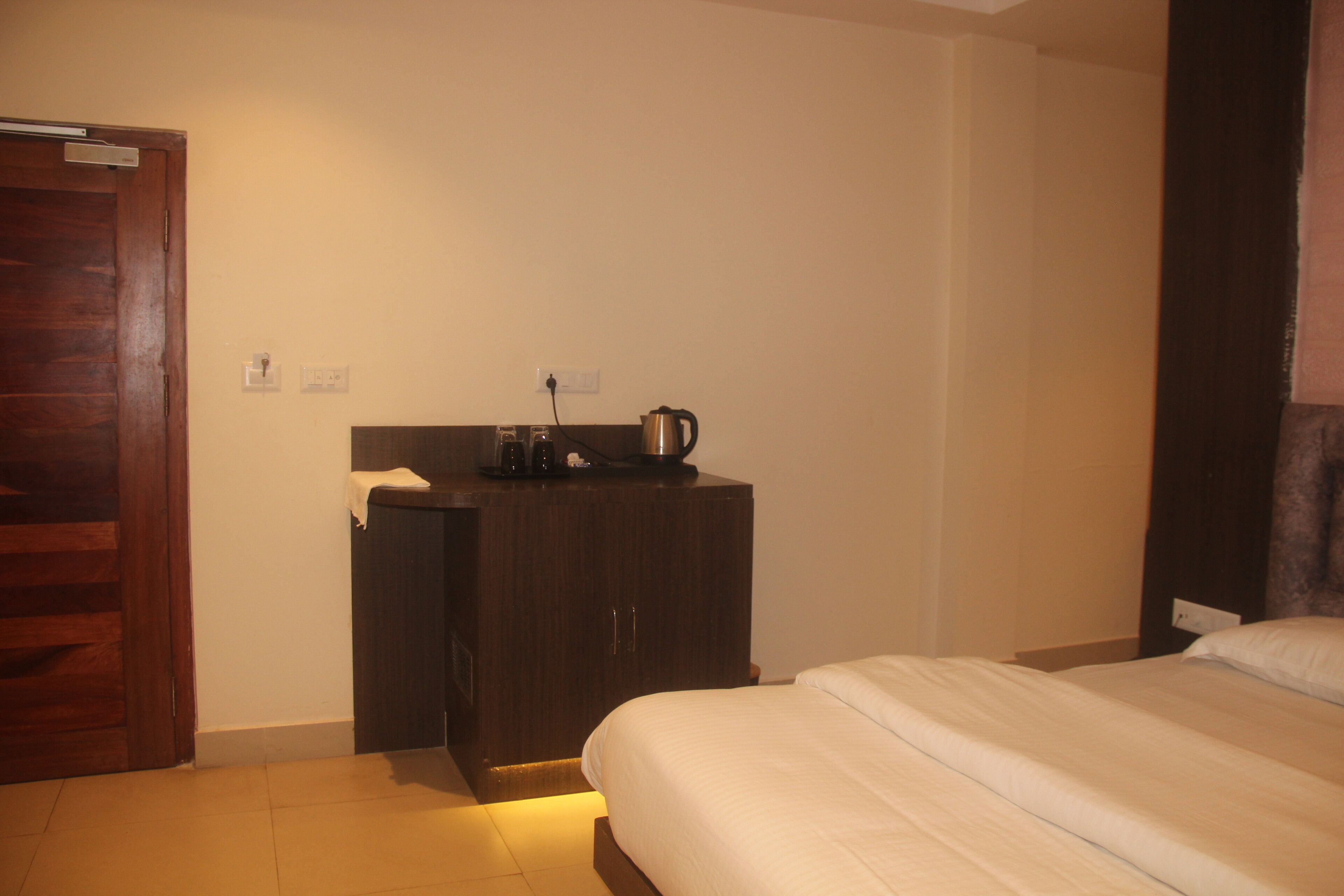 A hotel room with a bed, a wooden desk with a kettle, and a door.