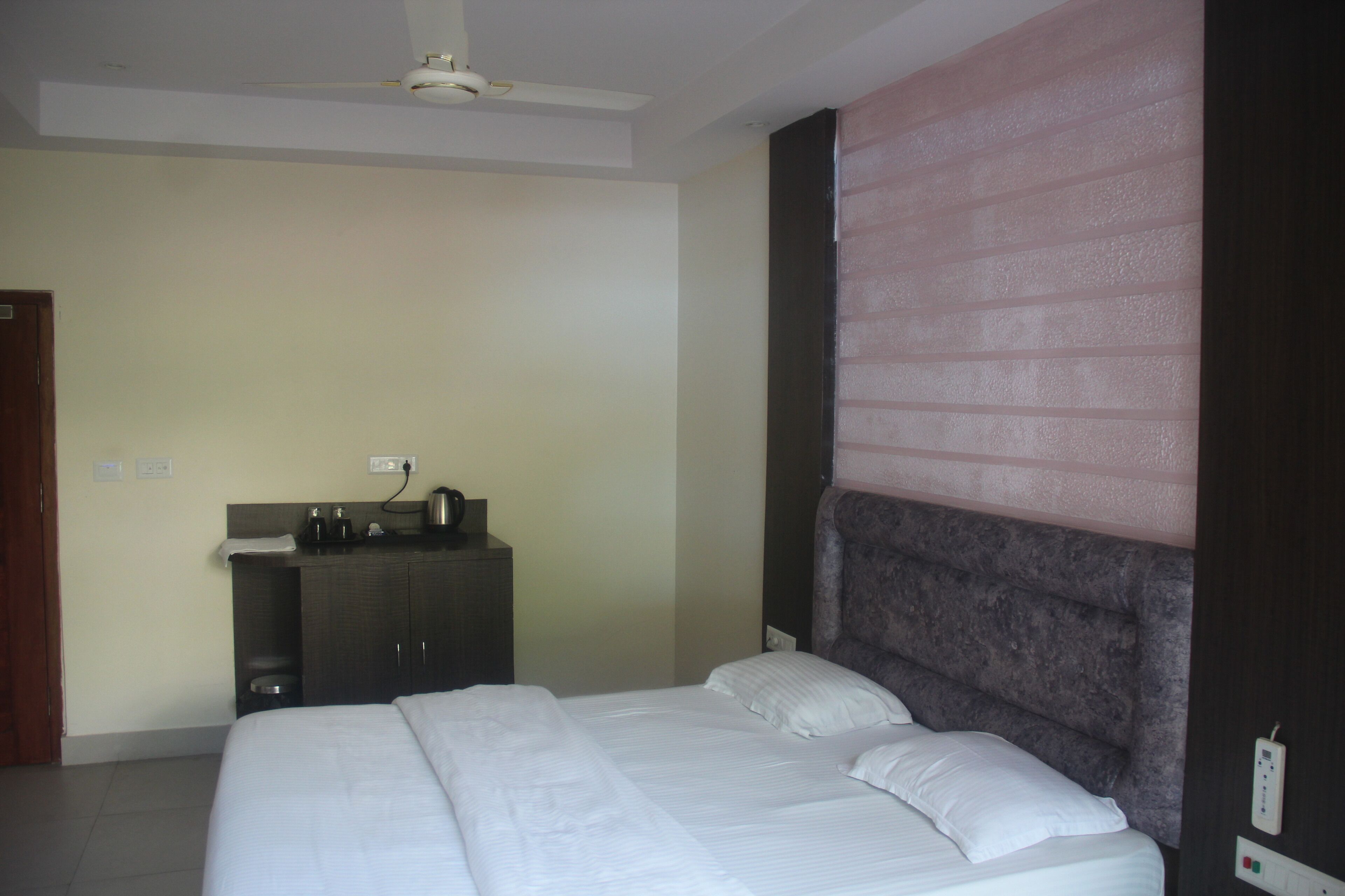 Quarto de hotel com cama, cômoda, ventoinha no teto e janela com persianas.