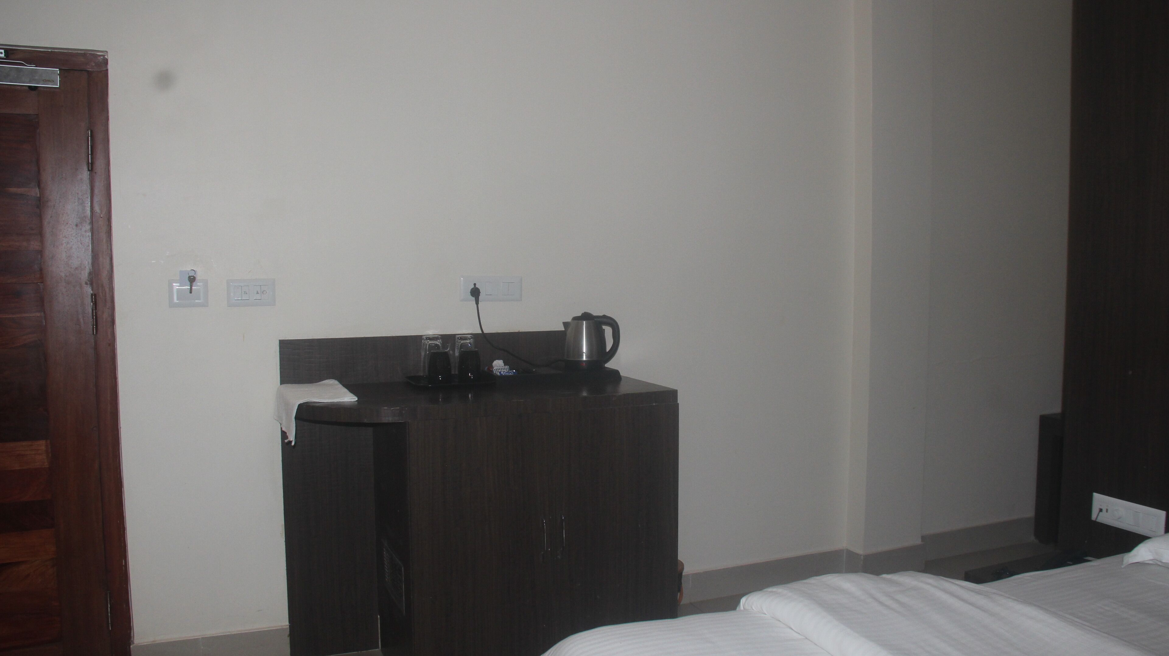A hotel room with a bed, a wooden desk with a kettle, and a small table.