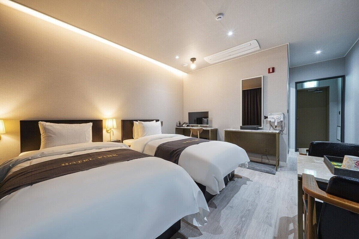A hotel room with two beds, a desk, a TV, and a mirror.