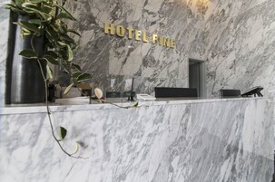 Un mostrador de recepción de mármol con un letrero que dice "HOTEL FINE" y una planta a la izquierda.