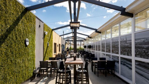 Une terrasse extérieure avec des tables et des chaises, un mur végétal et de grandes fenêtres offrant une vue sur la ville.