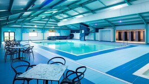 Une piscine intérieure dont le sol est recouvert de carreaux bleus et blancs, entourée de chaises et de tables noires.