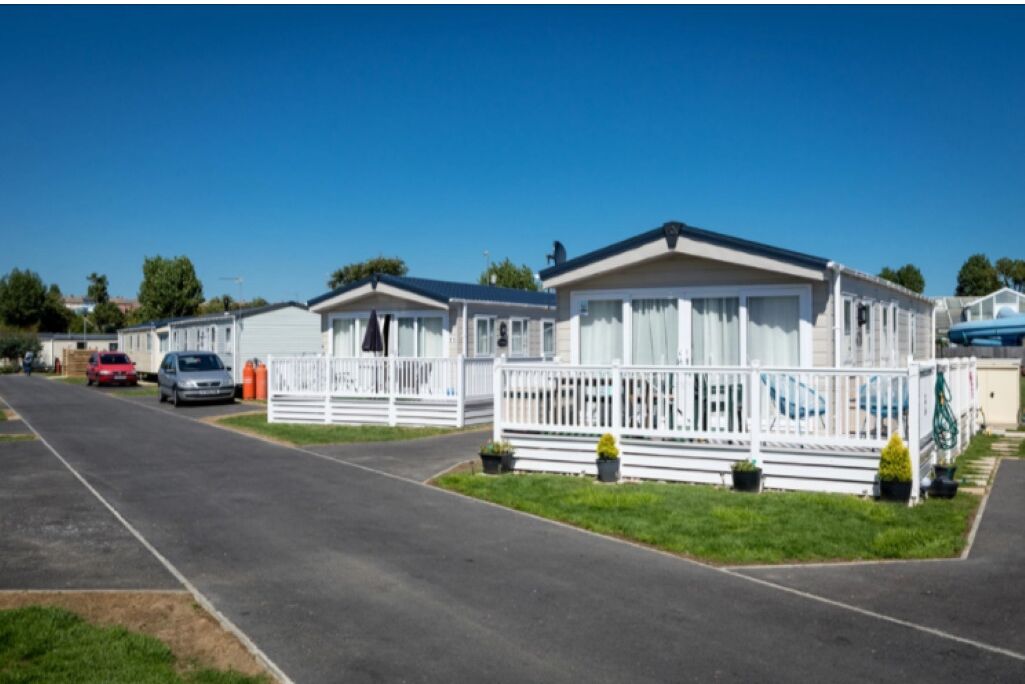 A row of mobile homes with white railings and a paved road in front.