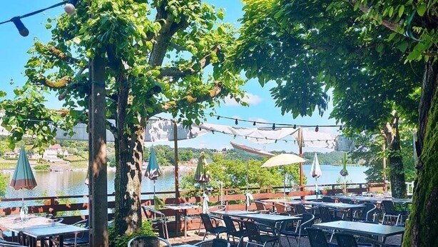 An outdoor dining area with tables and chairs, surrounded by trees and overlooking a body of water. - Lake view Lodge chambon Eguzon  <br>Beautiful  Lake Views  (Éguzon-Chantôme)