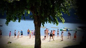 A group of people walking on a beach near a lake, with a tree in the foreground and boats in the water. - Lake view Lodge chambon Eguzon  <br>Beautiful  Lake Views  (Éguzon-Chantôme)