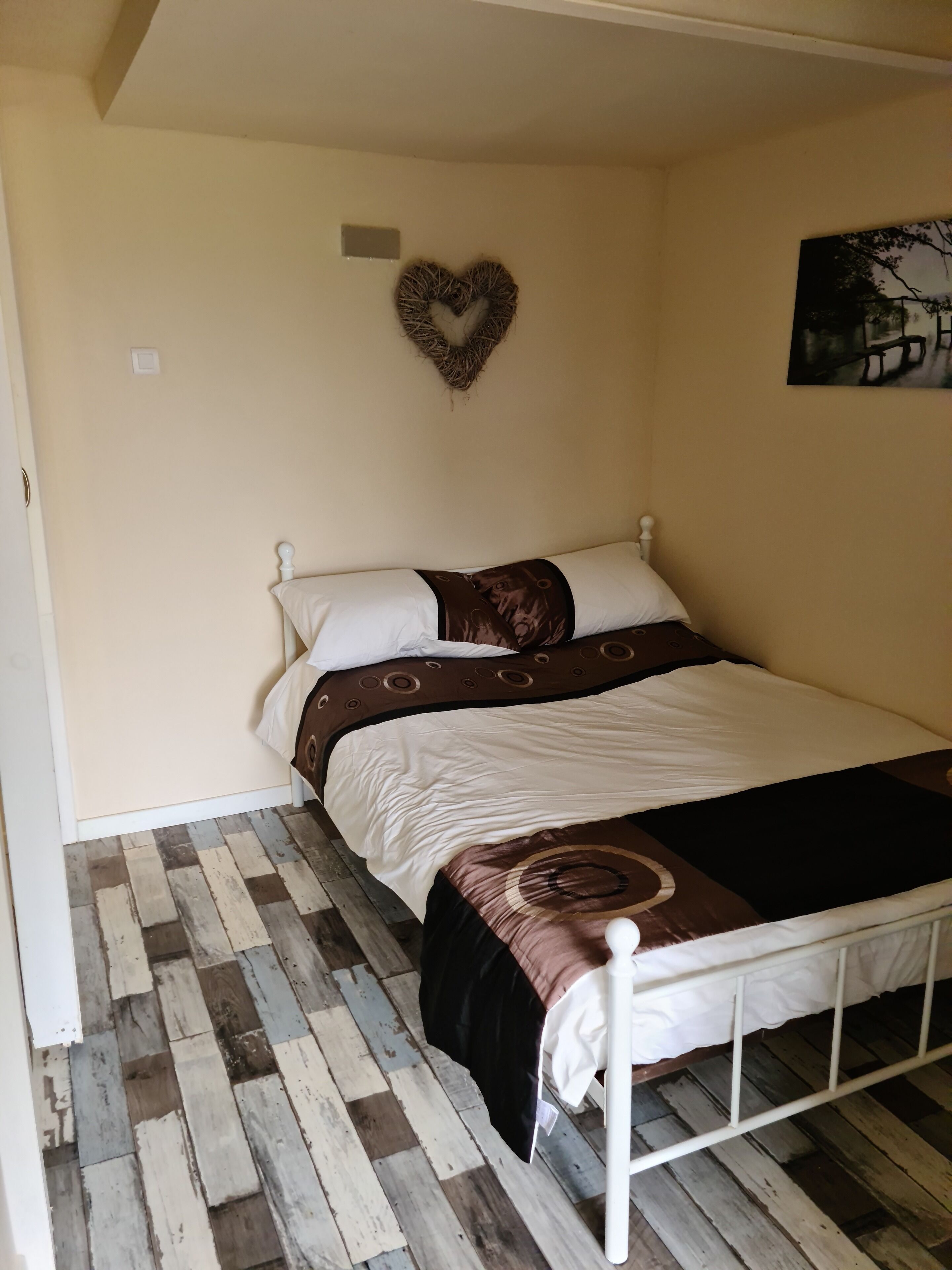 A single bed with a white frame, a patterned bedspread, and a heart-shaped decoration on the wall.