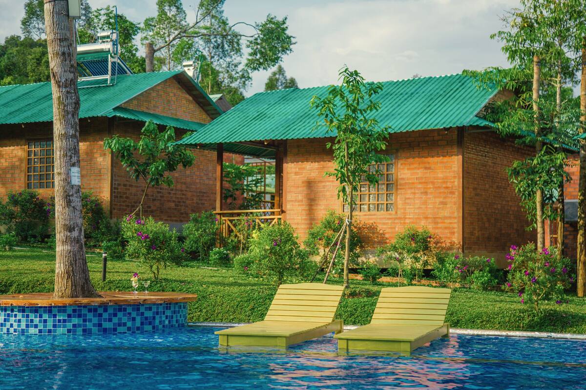 A poolside area with two lounge chairs, a brick building with a green roof, and a small garden with various plants and flowers.