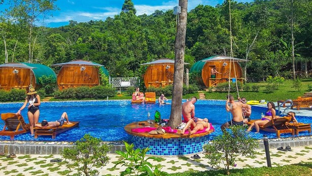 A pool area with wooden cabanas, lounge chairs, and a central circular platform. - Valley Sen Bungalow (Phu Quoc)