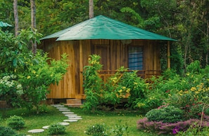 A wooden cabin with a green roof surrounded by lush greenery and a stone pathway leading to it. - Valley Sen Bungalow (Phu Quoc)