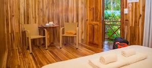 A wooden room with a bed, two wicker chairs, a small table with a cup and a book, and a suitcase. - Valley Sen Bungalow (Phu Quoc)