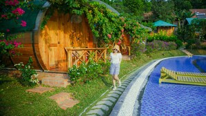 A wooden cabin with a porch, surrounded by lush greenery and a swimming pool. - Valley Sen Bungalow (Phu Quoc)