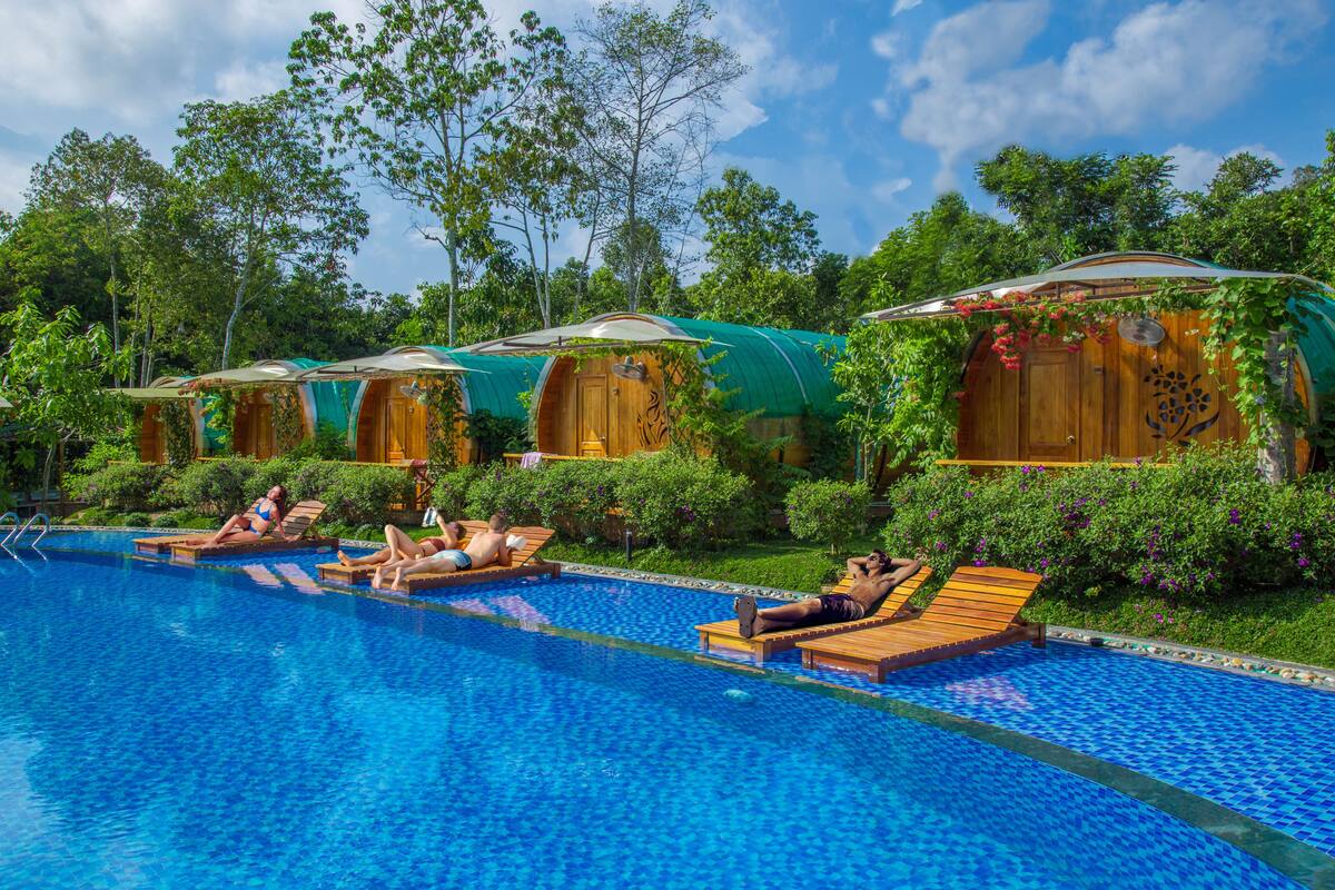 A pool area with wooden cabanas and lounge chairs.