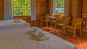 A room with two beds, a small table with chairs, and a view of greenery through the windows. - Valley Sen Bungalow (Phu Quoc)