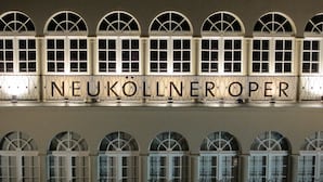 The exterior of the Neuköllner Opera building with arched windows and a sign reading "NEUKÖLLNER OPER".