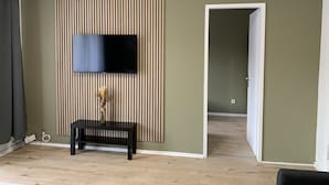 A room with a flat-screen TV mounted on a striped wall, a bench, and a door leading to another room.