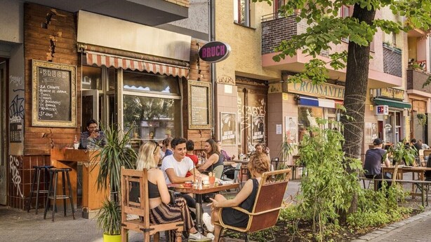 An outdoor café with wooden tables and chairs, a chalkboard menu, and a sign reading "BRUCH".