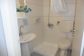 A bathroom with a pedestal sink, a toilet, a shower area, and a small shelf with a vase of flowers. - Julie's studio,2 minutes walk to beach, near Heraklion,Knossos and famous sites! (Kokkini Hani)