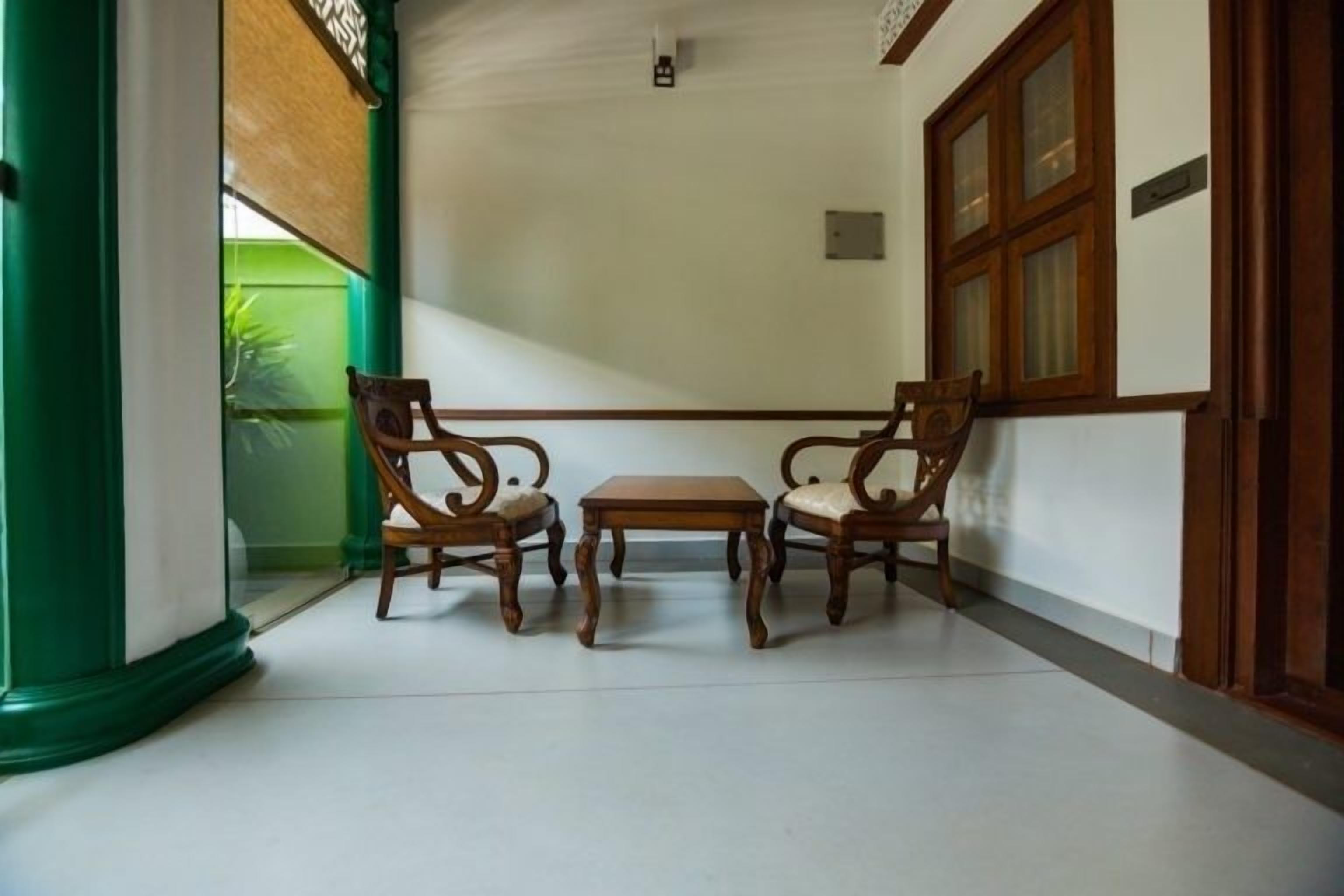 Una habitación con una mesa de madera y dos sillas, un pilar verde y un ventanal con marcos de madera.