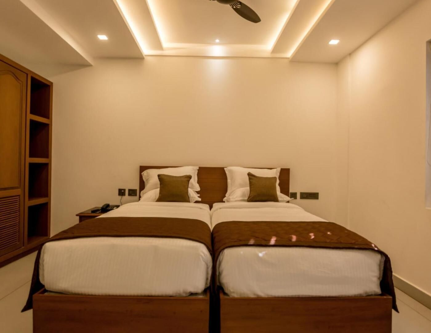 Een tweepersoonsbed met een houten hoofdbord, twee nachtkastjes en een plafondventilator.