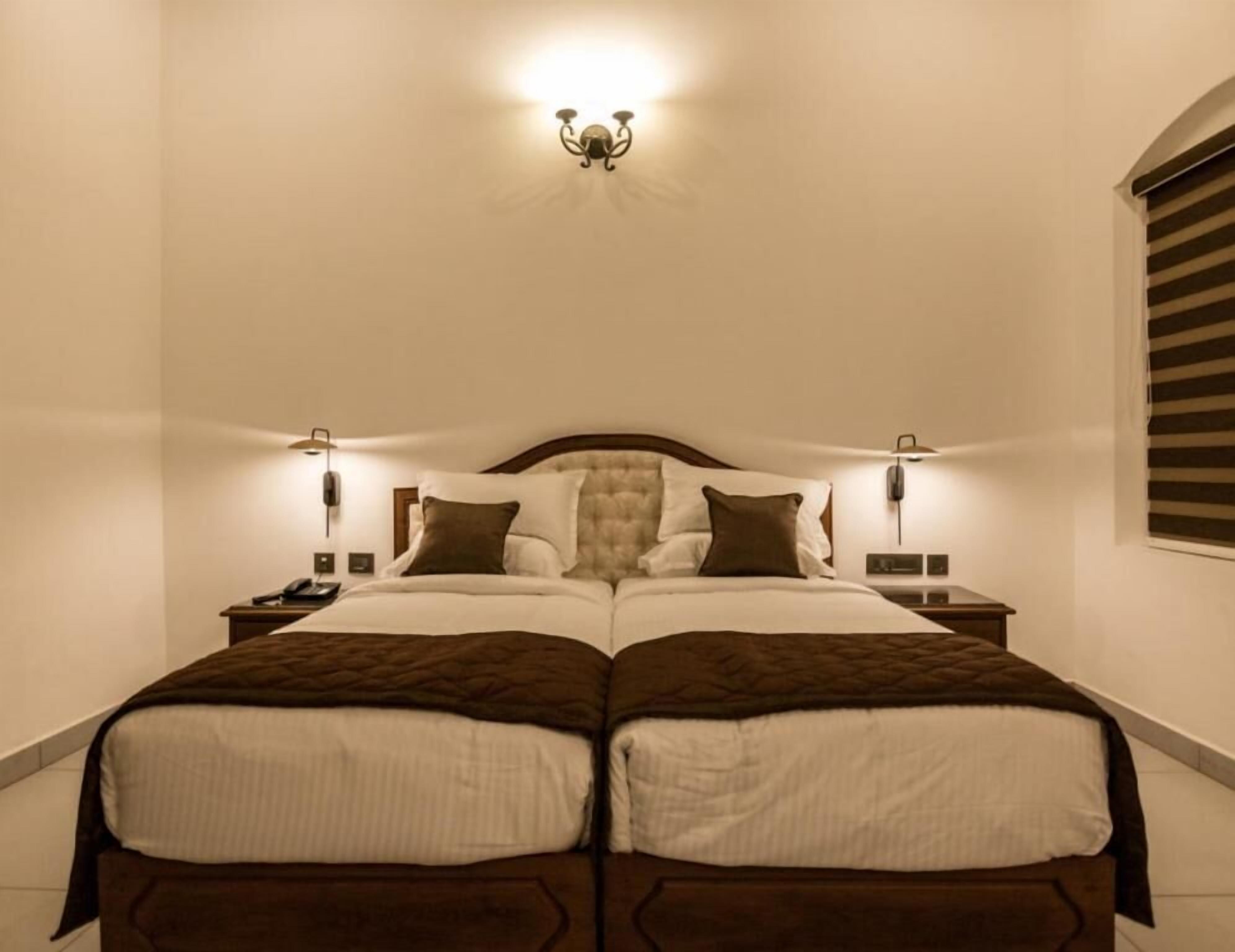 A double bed with a tufted headboard, two bedside tables with lamps, and a wall-mounted light fixture.