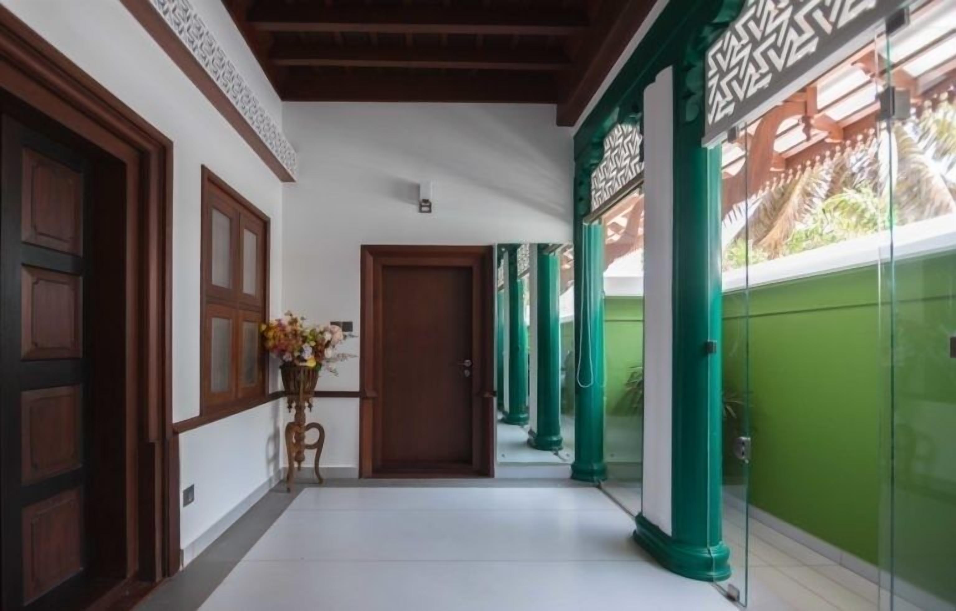A corridor with wooden doors, a potted plant, and green pillars.