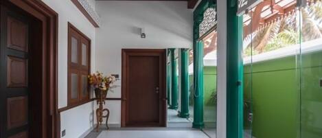 A corridor with wooden doors, a potted plant, and green pillars.