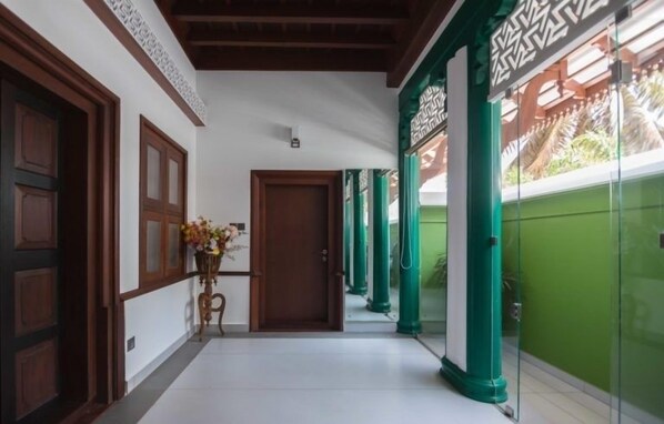 A corridor with wooden doors, a potted plant, and green pillars. - Villa De 1945 (Mahe)
