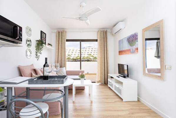 Una sala de estar moderna con comedor, sofá, televisor y balcón con vistas a edificios.