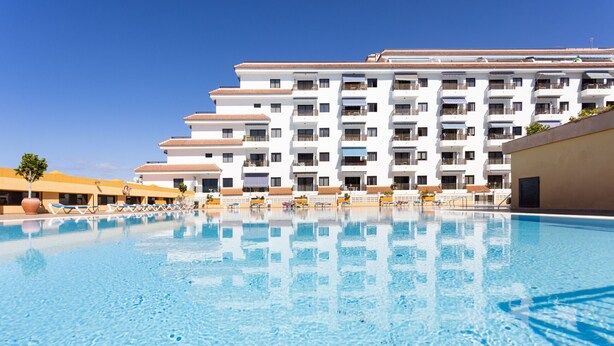 Un hotel con piscina, varios balcones y un cielo azul despejado.