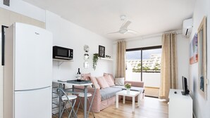Un apartamento moderno con cocina, comedor y sala de estar. Cuenta con refrigerador, microondas, mesa de comedor, sofá y televisor.