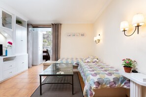 Een ruime, goed verlichte kamer met een bed, een glazen tafel, een bank en een televisie.